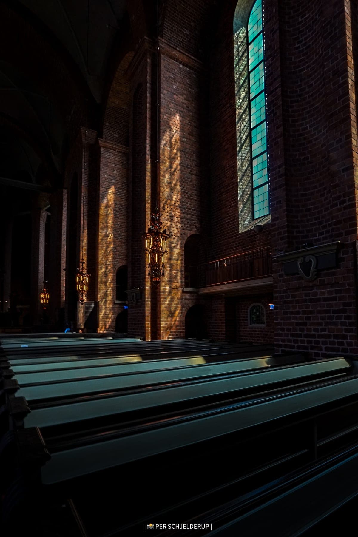 Rows of empty church pews beneath brick arches and a stained-glass window.